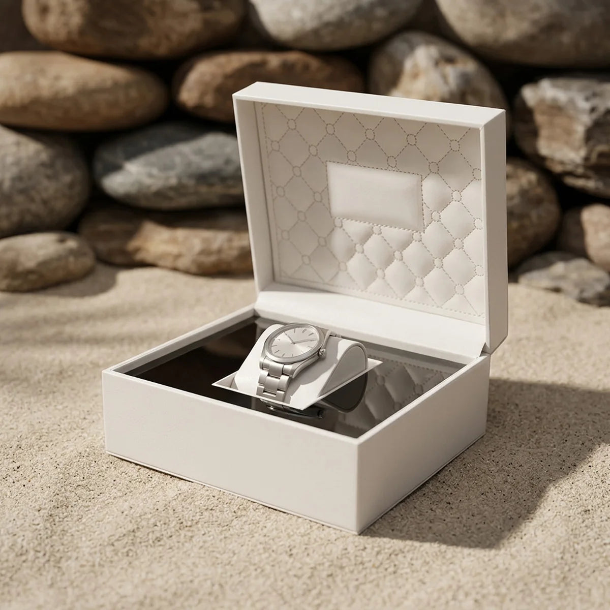 Boîte à montre Le Matelassé, coque ivoire et intérieur matelassé posée sur le sable