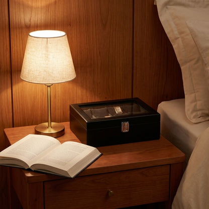 Le Comptoir VIII noir sur une table de nuit en bois, éclairé par une lampe de chevet