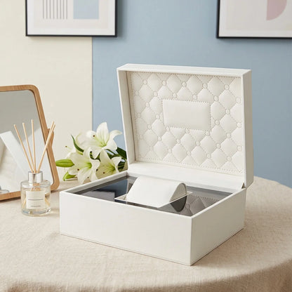 Boîte à montre Le Matelassé, coque ivoire et intérieur matelassé sur une table à côté d'un diffuseur de parfum et d'un miroir