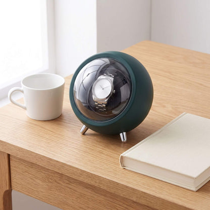Remontoir de montre La Capsule posé sur une table de chevet en bois, à côté d'une tasse et d'un livre