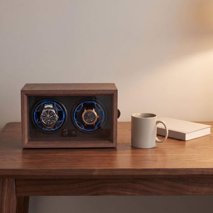 Remontoir deux montres de 24,5 cm de large sur un bureau, à côté d'une tasse et d'un livre