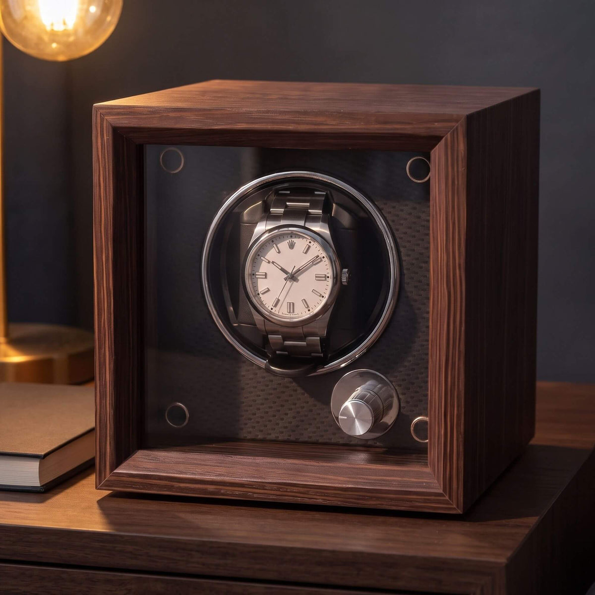Le Cube sur une table de chevet éclairée par une lampe, montre automatique en place derrière la vitre